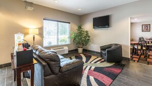 Een moderne woonkamer met een leren bank, een flatscreen televisie, een potplant en een eethoek met stoelen en tafels.