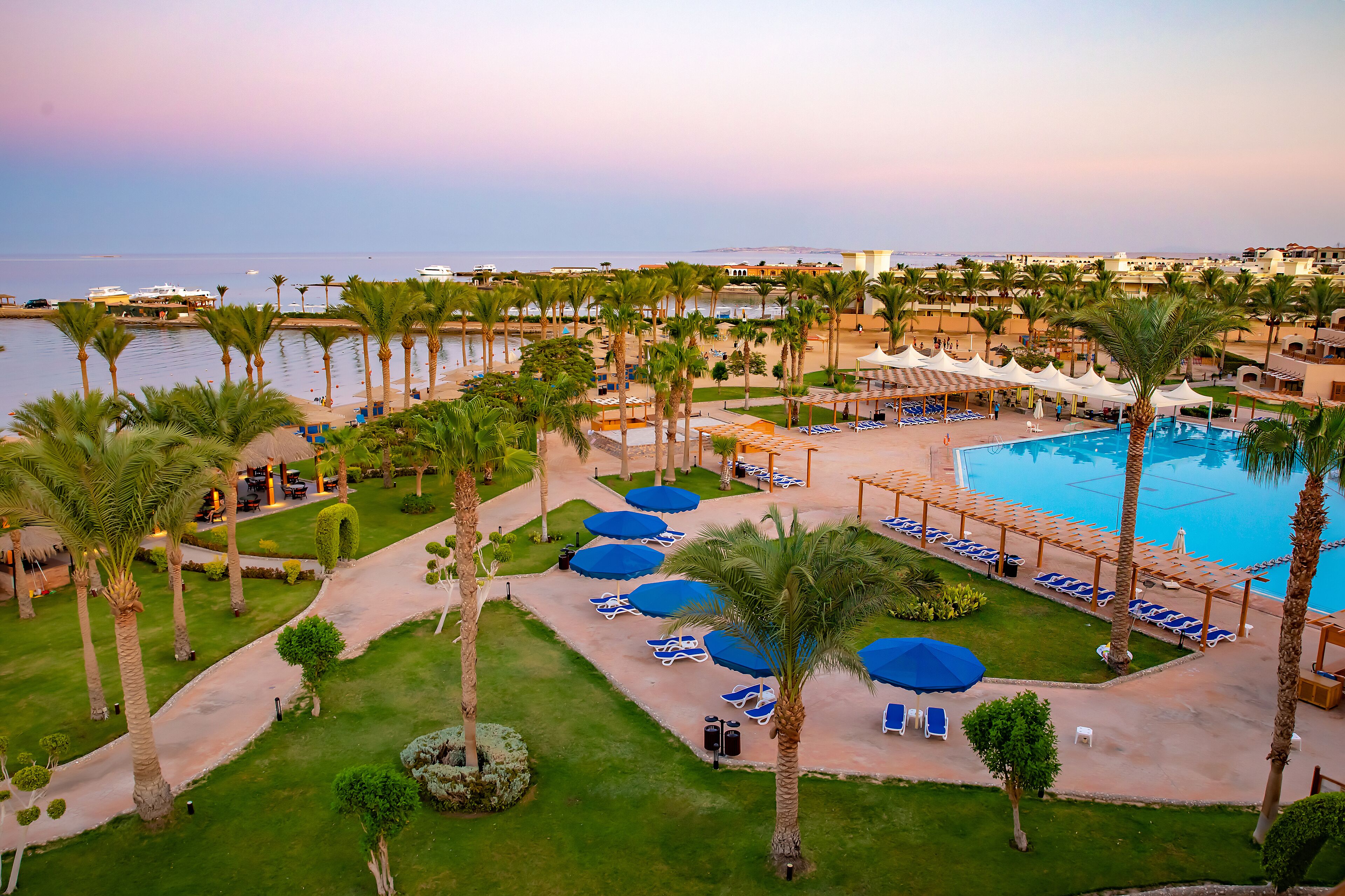 A resort with a swimming pool, palm trees, and beach umbrellas.