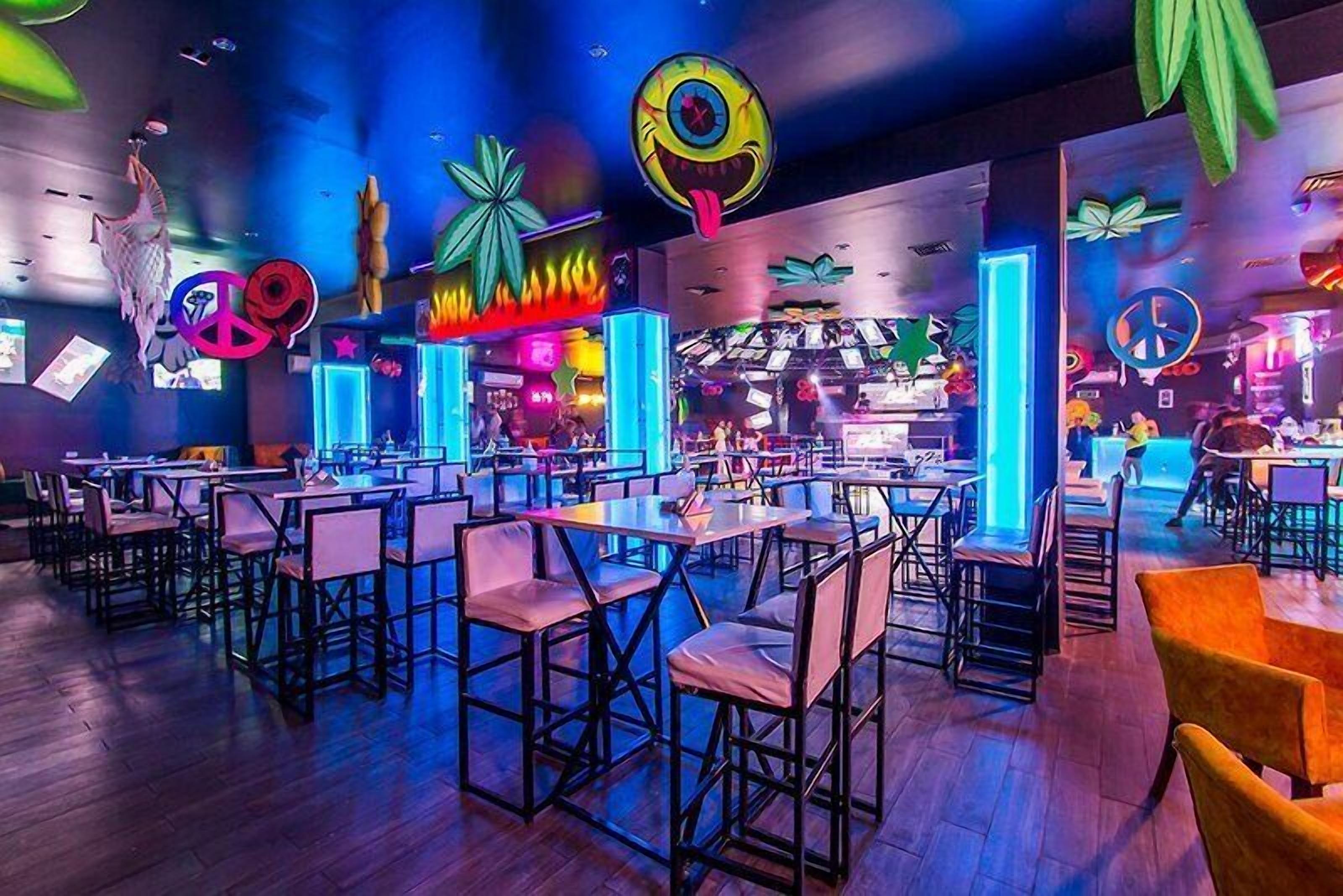 A vibrant indoor space with multiple tables and chairs, neon signs, and decorative elements.