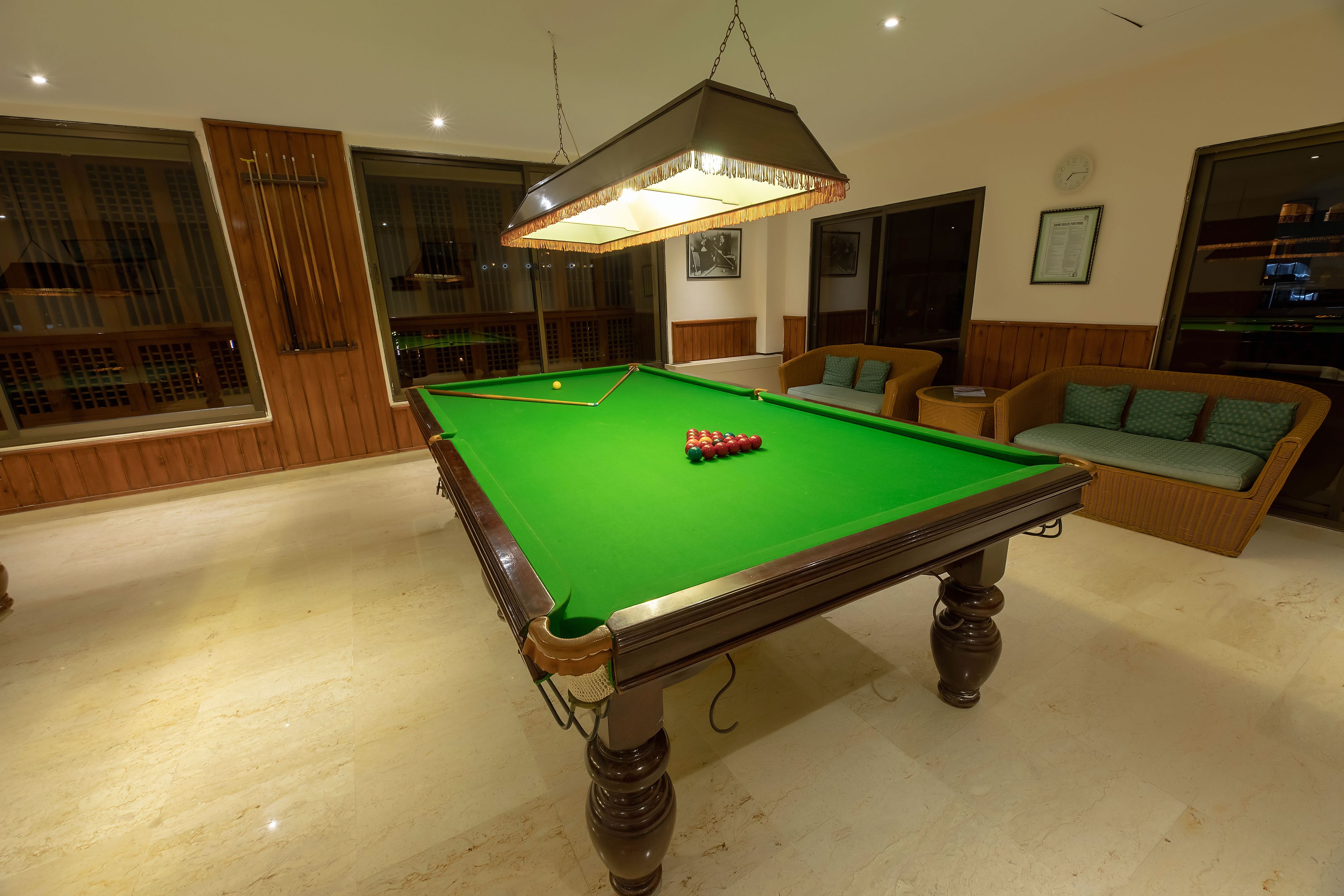 A pool table in a room with wooden paneling, a hanging lamp, and a sofa with cushions.