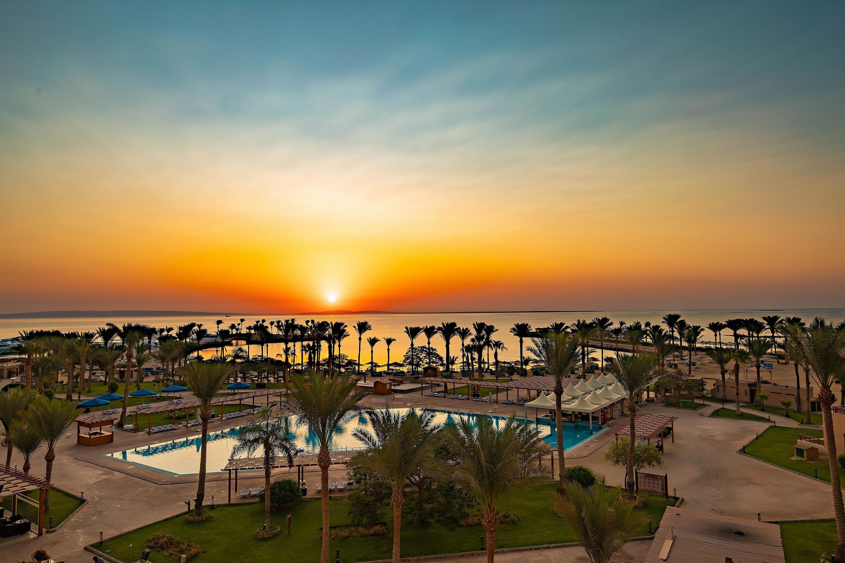 Un complexe hôtelier doté d’une piscine, de palmiers et offrant une vue imprenable sur le coucher de soleil.