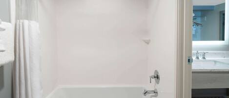 A bathroom with a white bathtub, a shower curtain, and a visible sink area in the background.