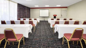 A conference room with rows of tables and chairs, a projector screen, and a podium.