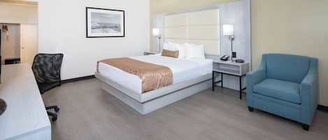 A hotel room with a large bed, a desk, a chair, and a bedside table with a lamp.