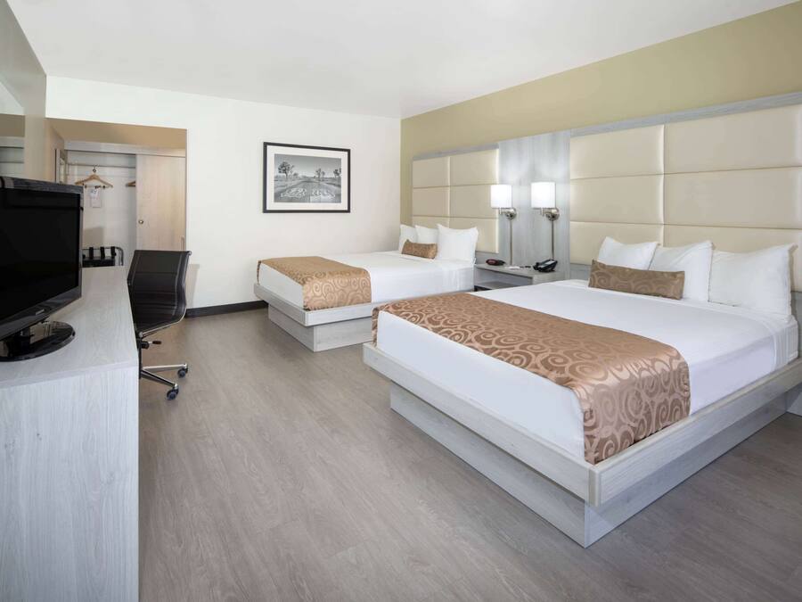 A hotel room with two beds, a desk with a television, and a framed picture on the wall.