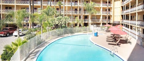 A hotel with a pool, multiple balconies, and palm trees.