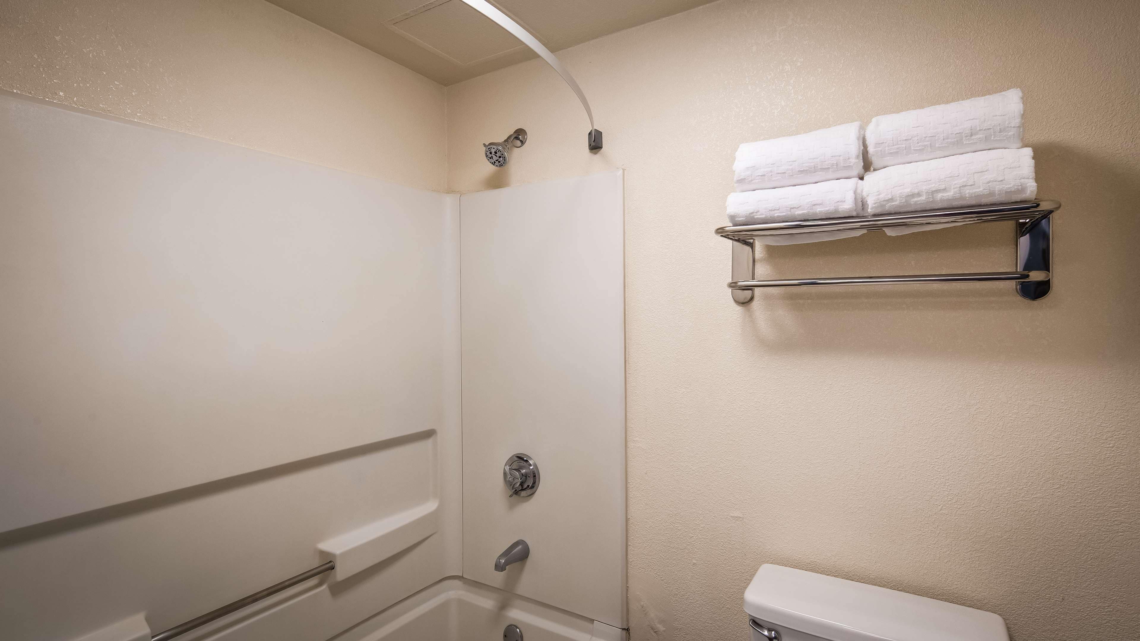 A bathroom with a shower, a toilet, and a towel rack with folded towels.