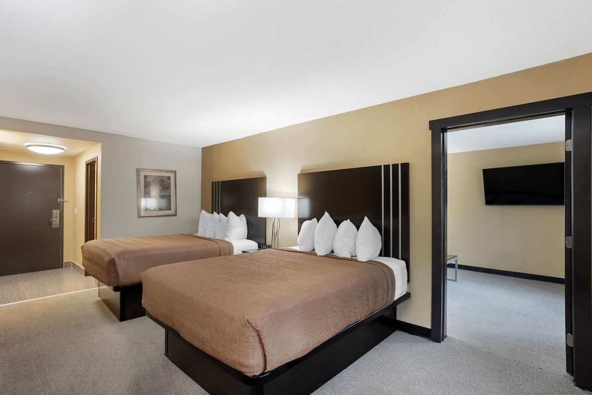 Habitación de hotel con dos camas, un televisor, una lámpara y una puerta que da a otra habitación.
