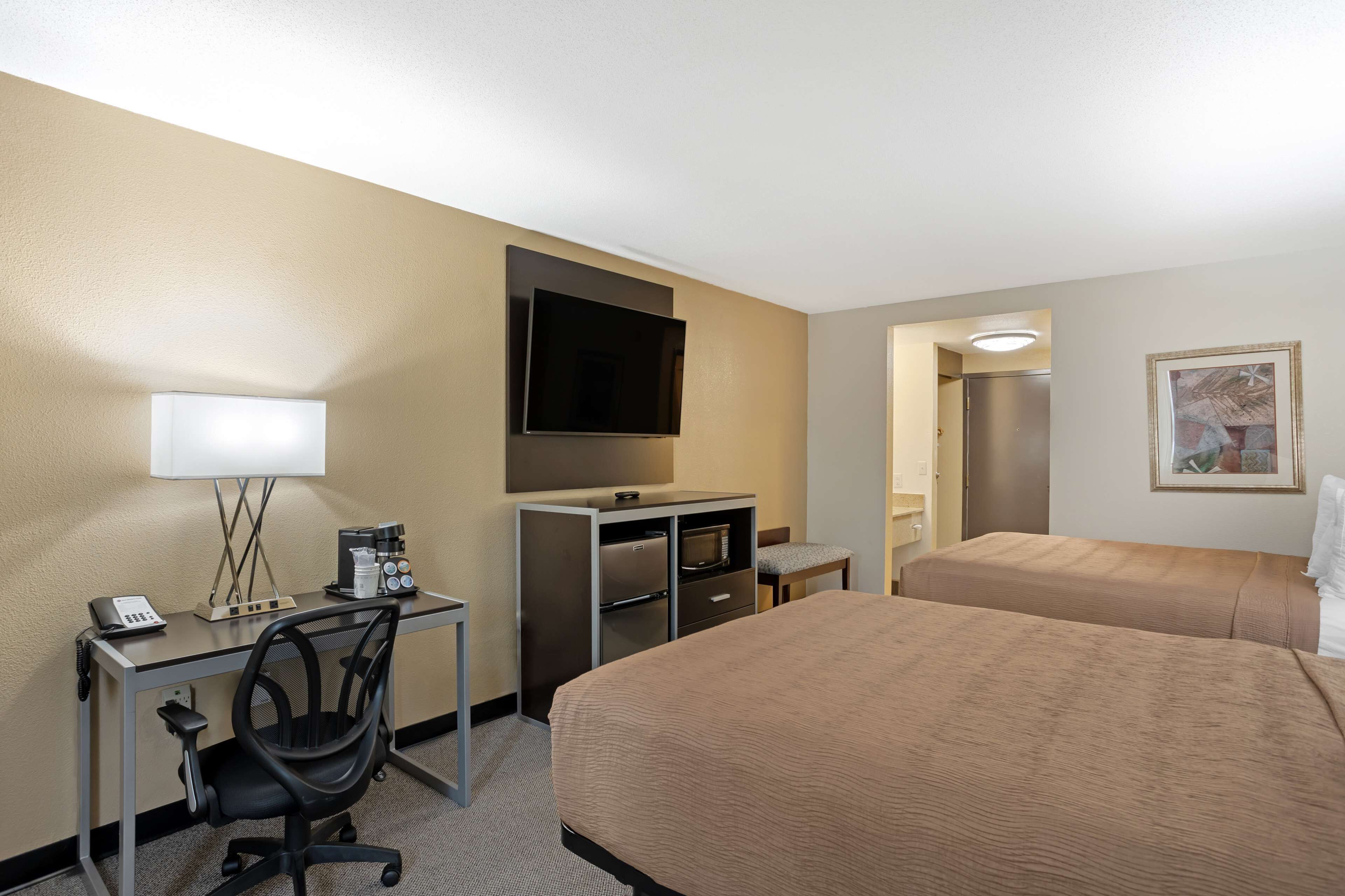 A hotel room with a desk, chair, bed, TV, and a painting on the wall.
