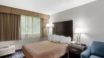 A hotel room with a bed, bedside table, lamp, and a chair.