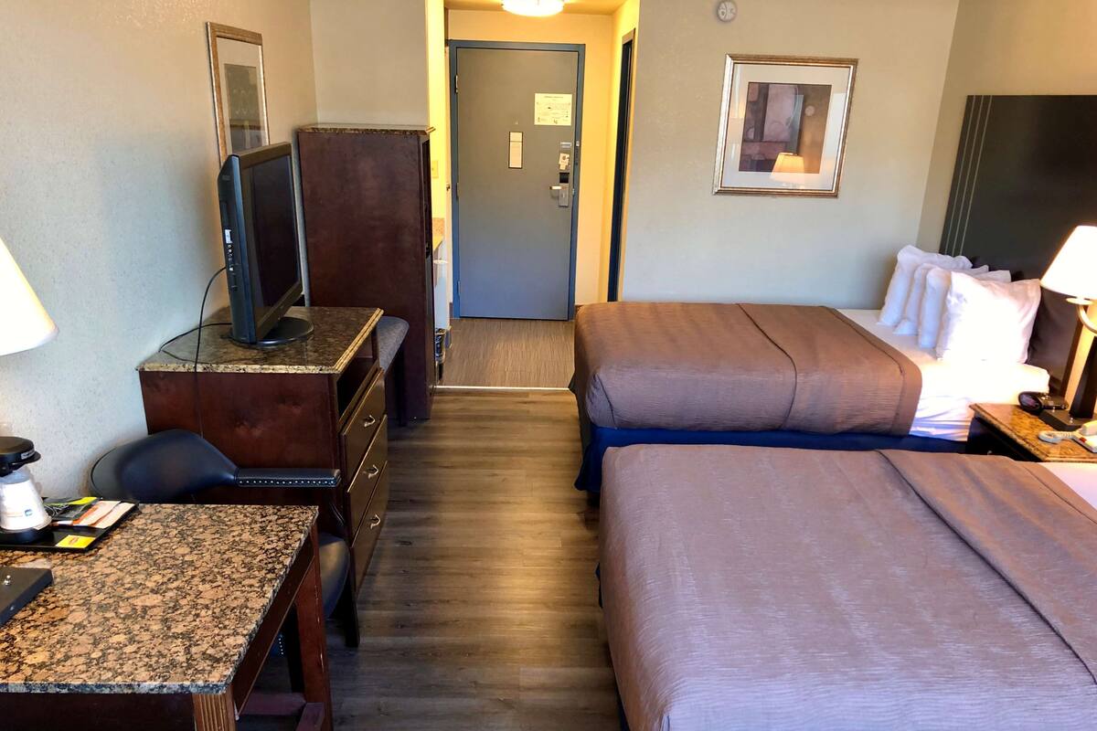 A hotel room with a desk, two beds, a TV, and a door leading to a hallway.