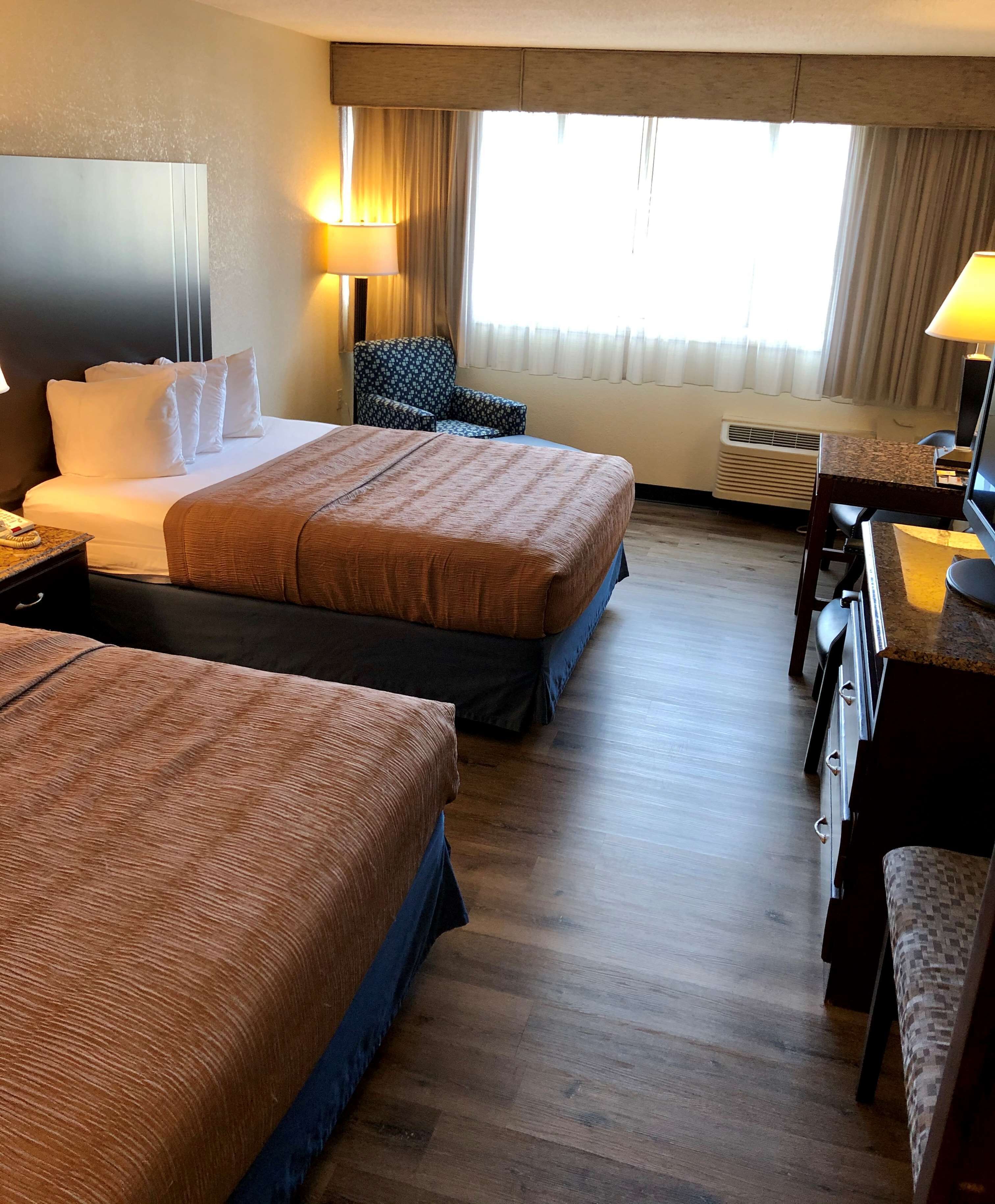 A hotel room with two beds, a desk, a chair, and a TV.