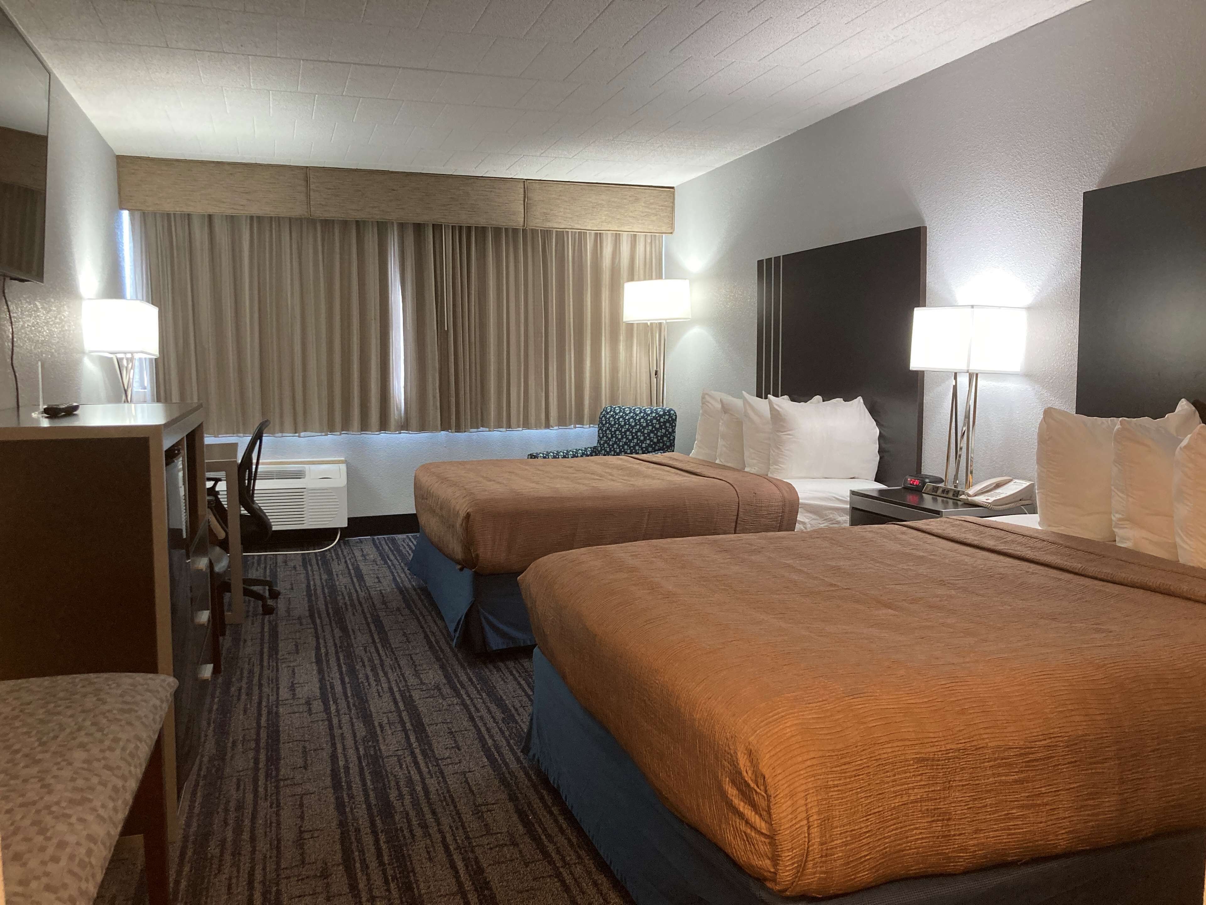 A hotel room with two beds, a desk, a chair, a lamp, and a window with curtains.