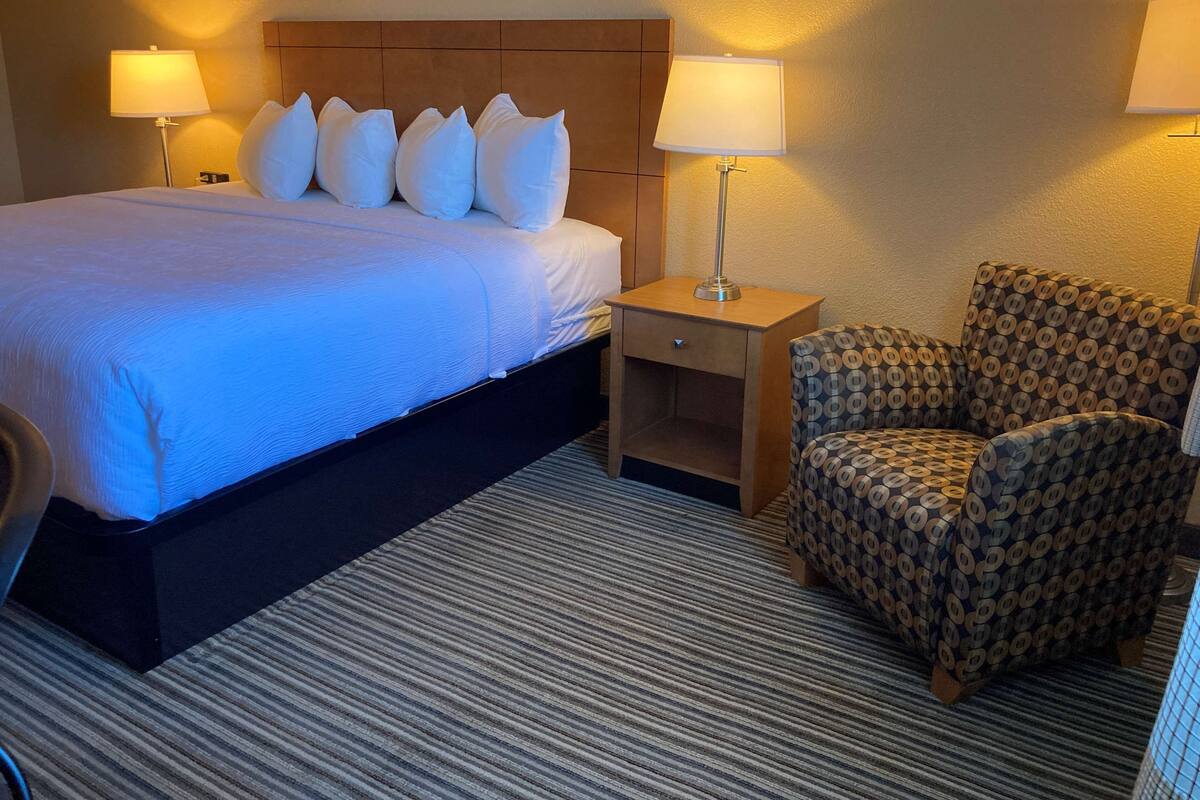 A hotel room with a large bed, a nightstand, a chair, and two lamps.