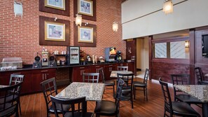 Um restaurante com parede de tijolos, obras de arte emolduradas, um balcão com máquinas de café e mesas com cadeiras.