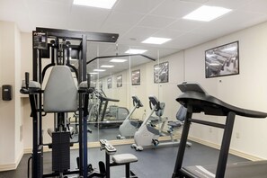Un gimnasio con equipo de ejercicio, cinta de correr y pared con espejos.