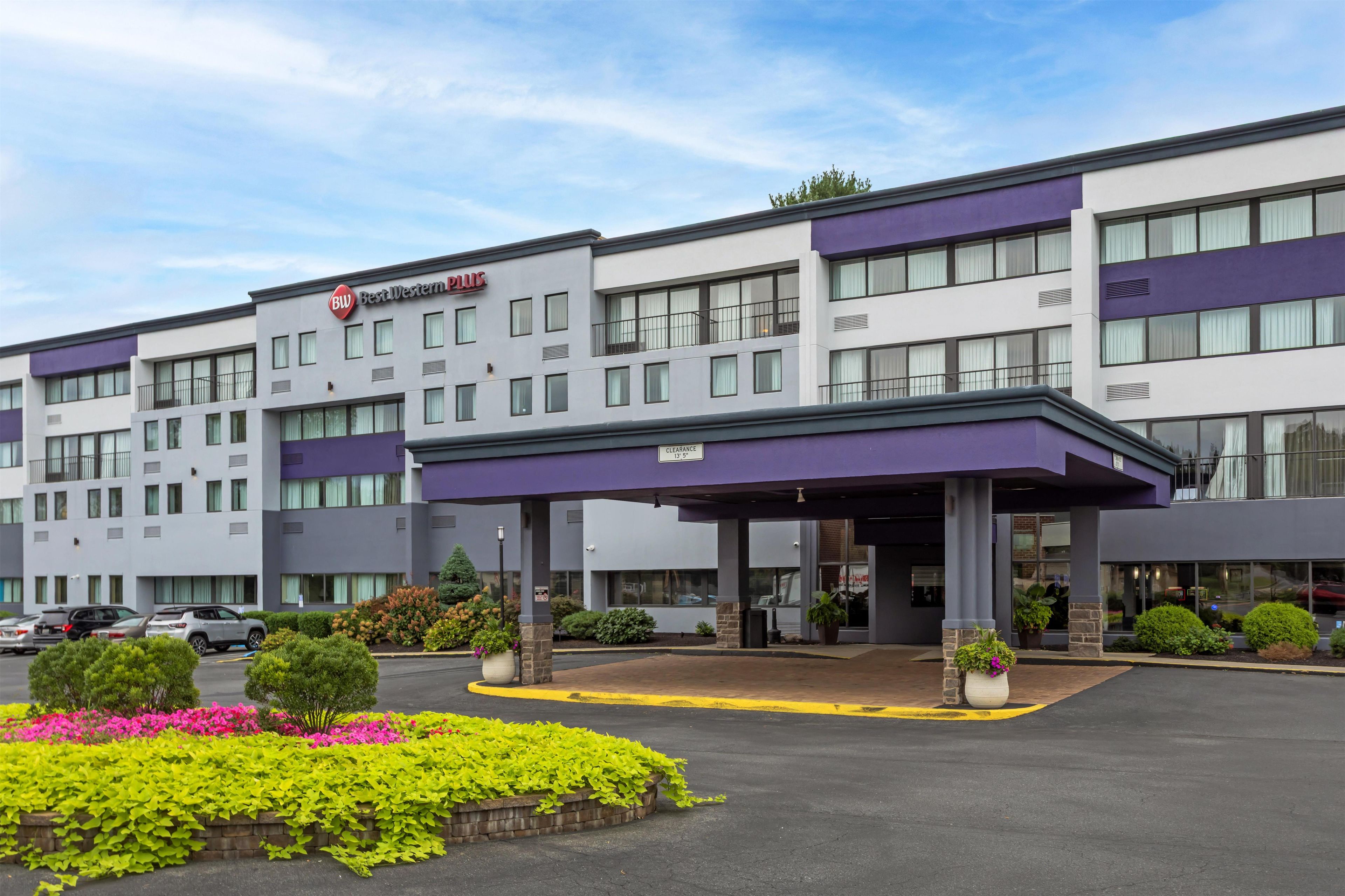 Ein Best Western Plus Hotel mit überdachter Eingangspartie, Parkplatz und angelegten Blumenbeeten.