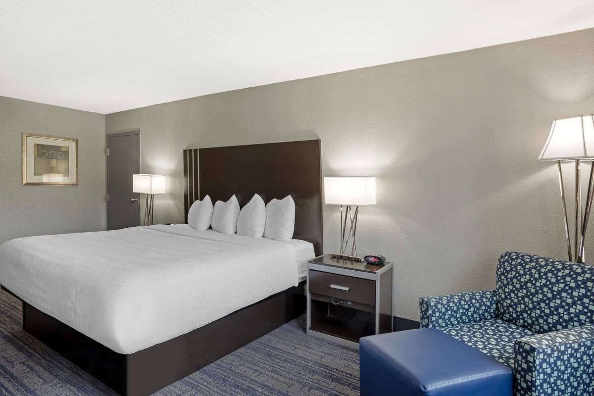 A hotel room with a large bed, bedside tables with lamps, a chair, and a small table.