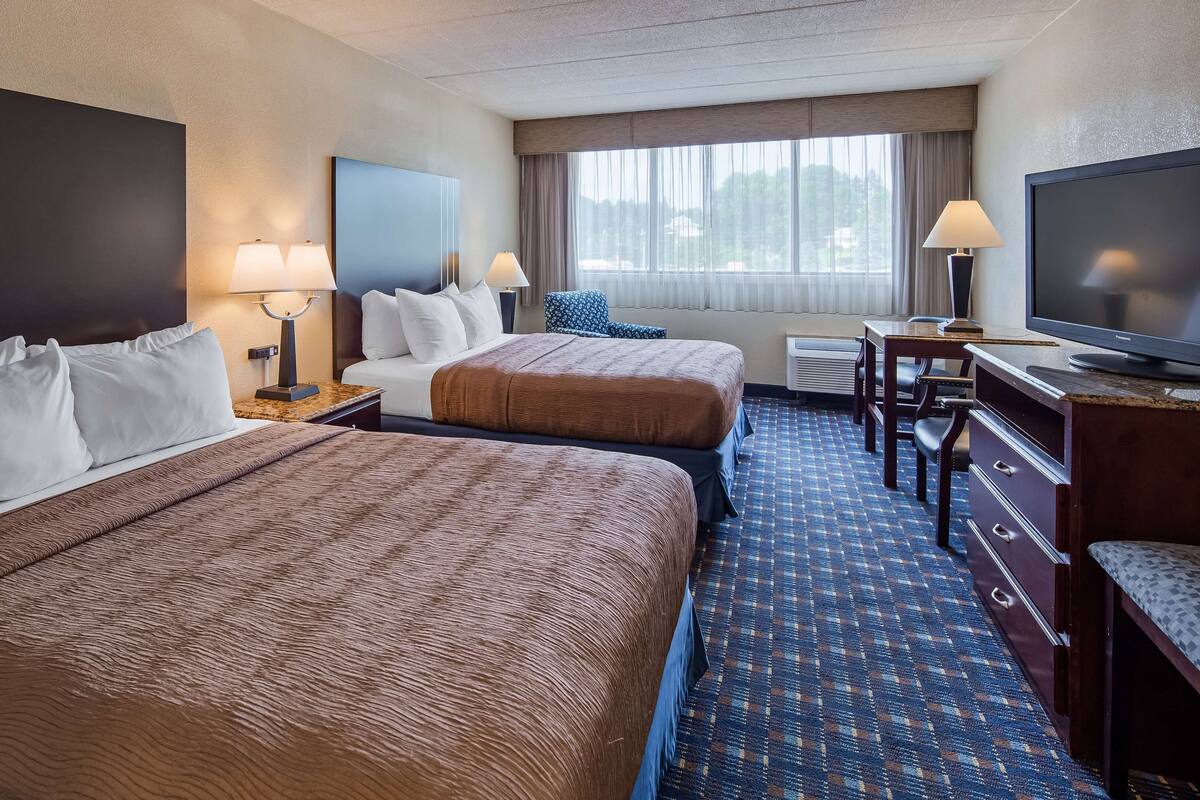 A hotel room with two beds, a TV, a desk, and a window with curtains.