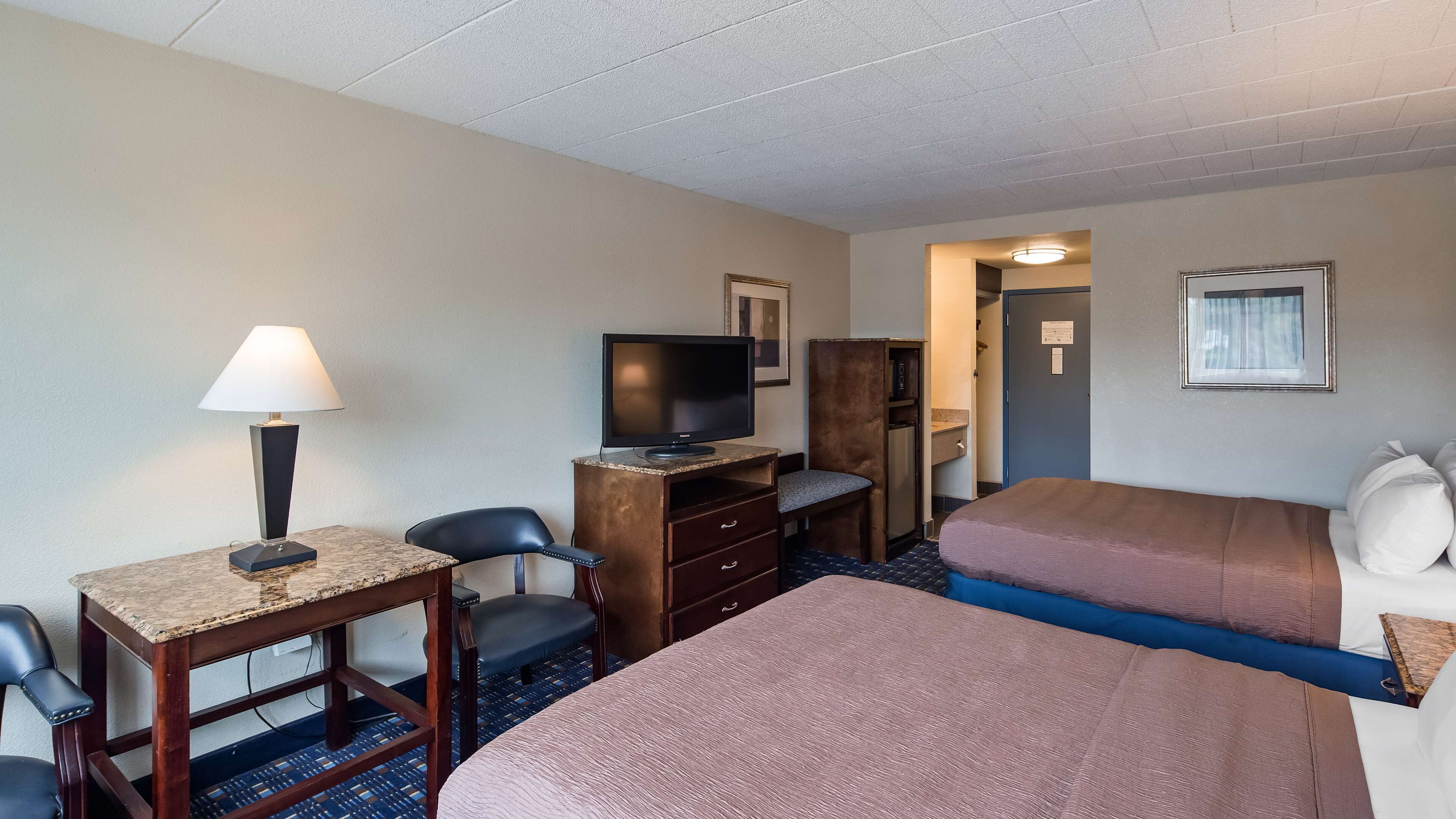 Habitación de hotel con escritorio, silla, televisión, cómoda y dos camas.
