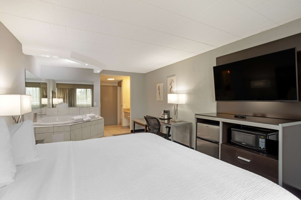 Habitación de hotel con una cama grande, un escritorio con silla, televisor, microondas y baño con espejo y lavamanos.