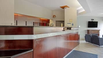 A reception area with a wooden counter, a flat-screen TV, and a seating area with sofas.