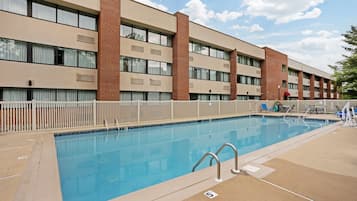 Una piscina rectangular con valla blanca, rodeada por un edificio con múltiples ventanas y pilares de ladrillo.