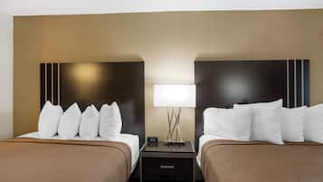 A hotel room with two beds, each with white pillows and brown bedding. There is a nightstand between the beds with a lamp and a clock displaying 10:52.