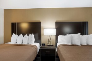 A hotel room with two beds, each with white pillows and brown bedding. There is a nightstand between the beds with a lamp and a clock displaying 10:52.