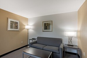 Habitación de hotel con un sofá gris, una mesita, dos lámparas y dos cuadros en las paredes.