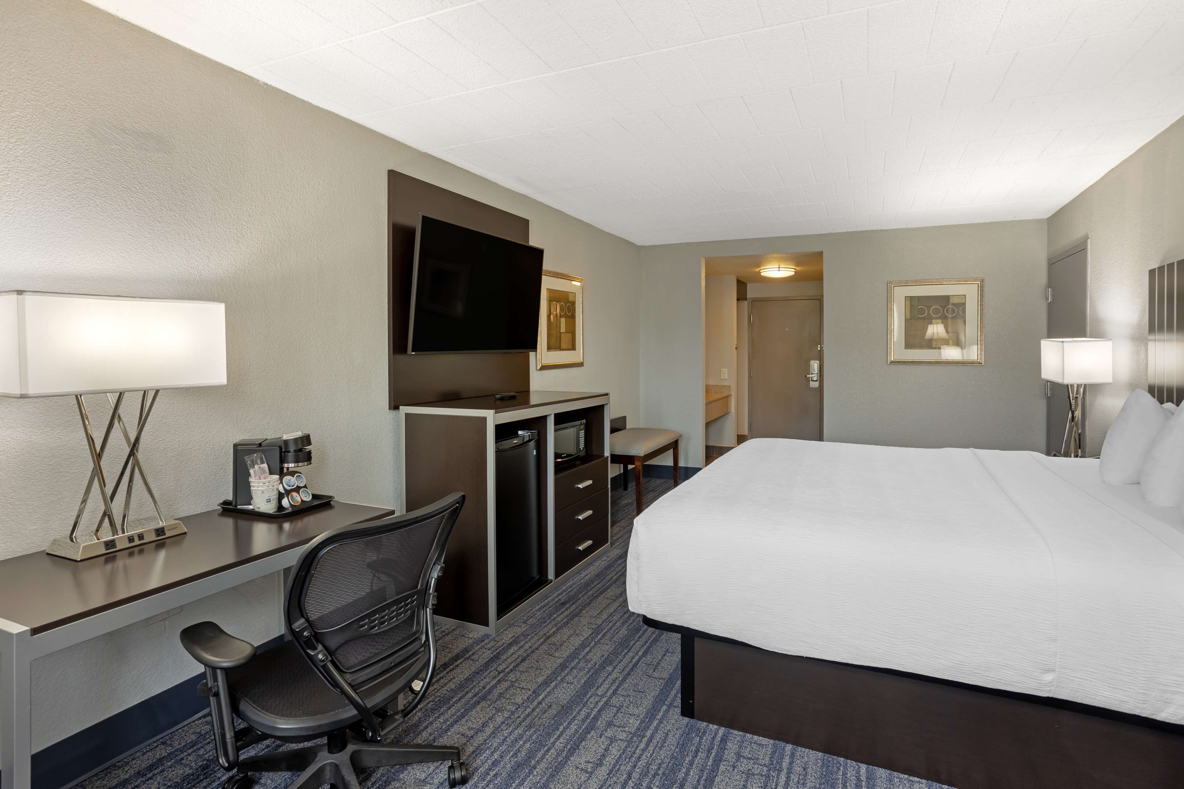 A hotel room with a large bed, a desk with a chair, a television, a coffee maker, and a minibar.