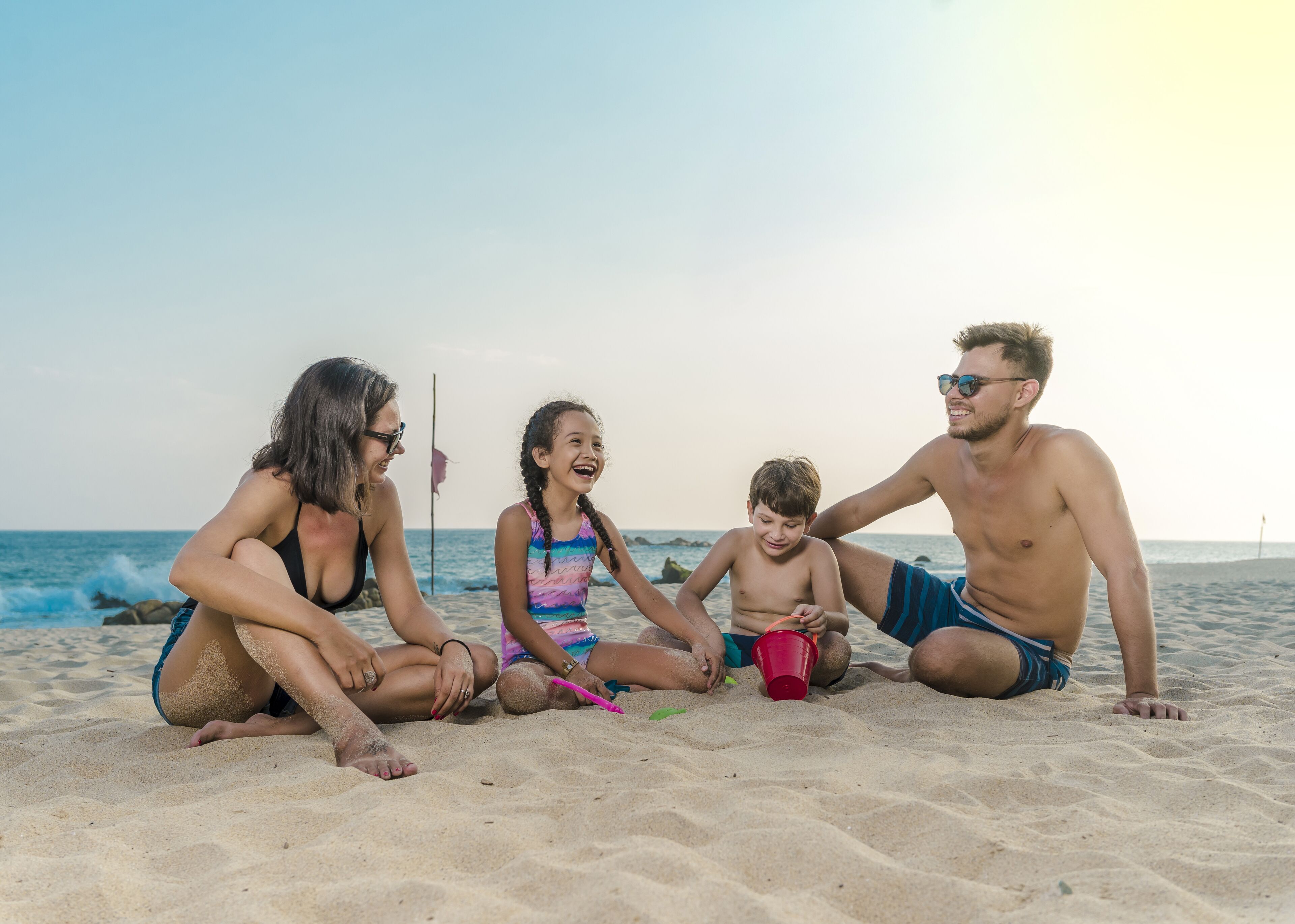 Una familia de cuatro personas sentada en una playa arenosa, con el océano al fondo.