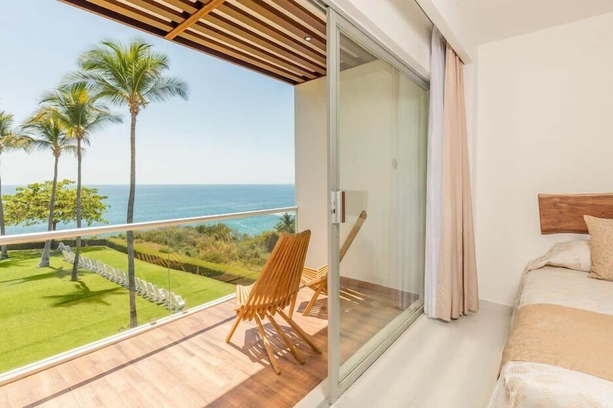 A balcony with a view of the ocean, a wooden chair, and a bed with a wooden headboard.
