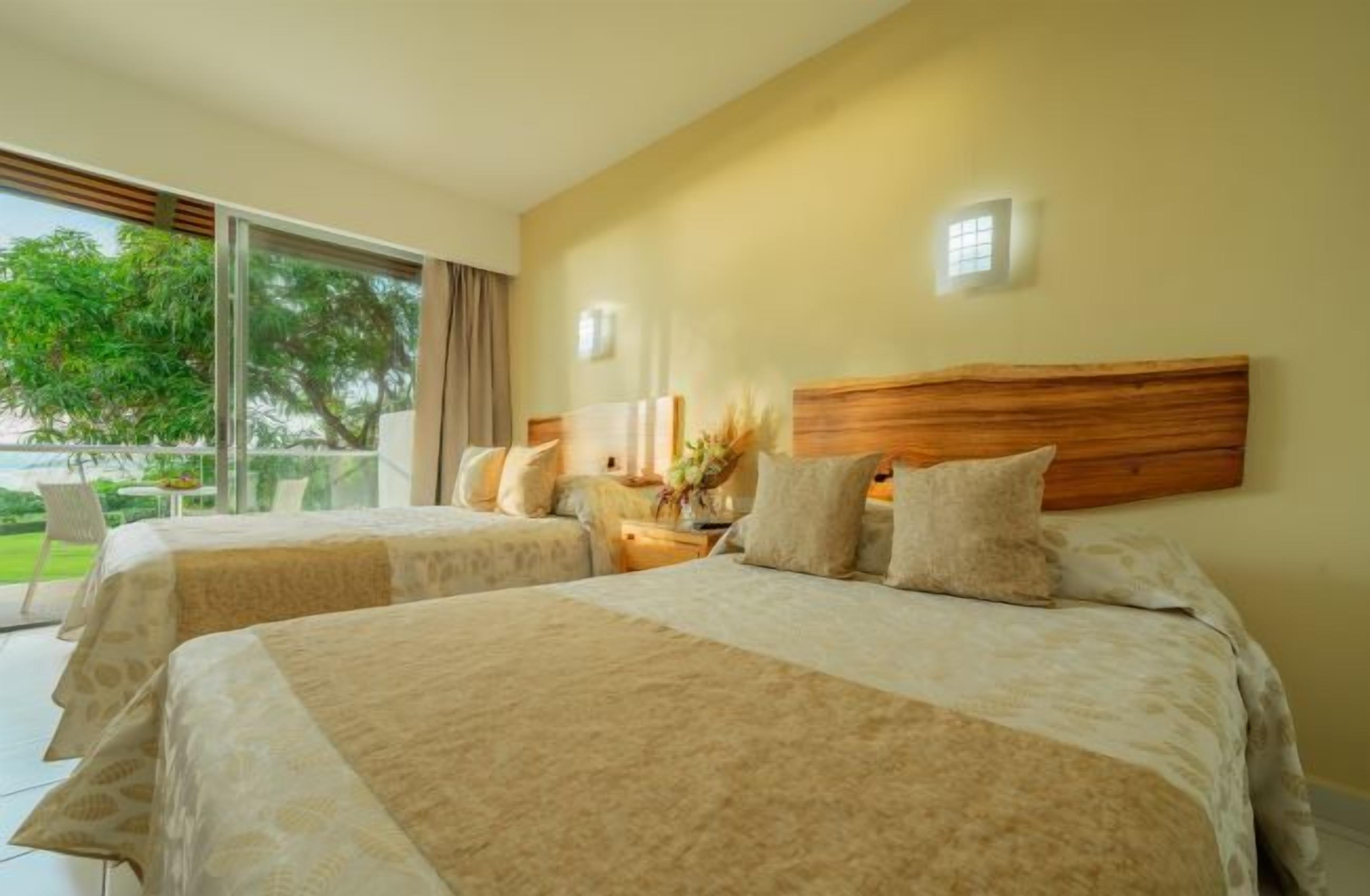 A hotel room with two beds, a large window, and a view of the outdoors.