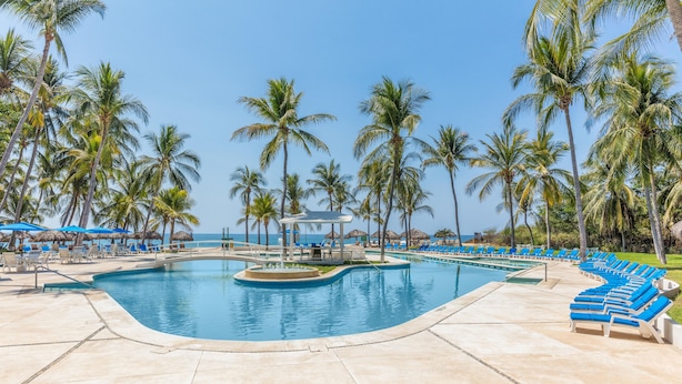 A pool area with lounge chairs and umbrellas, surrounded by palm trees and a clear view of the ocean. - Posada Real Puerto Escondido (Puerto Escondido)