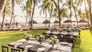 An outdoor dining area with tables set for a meal, surrounded by palm trees and overlooking the ocean. - Posada Real Puerto Escondido (Puerto Escondido)