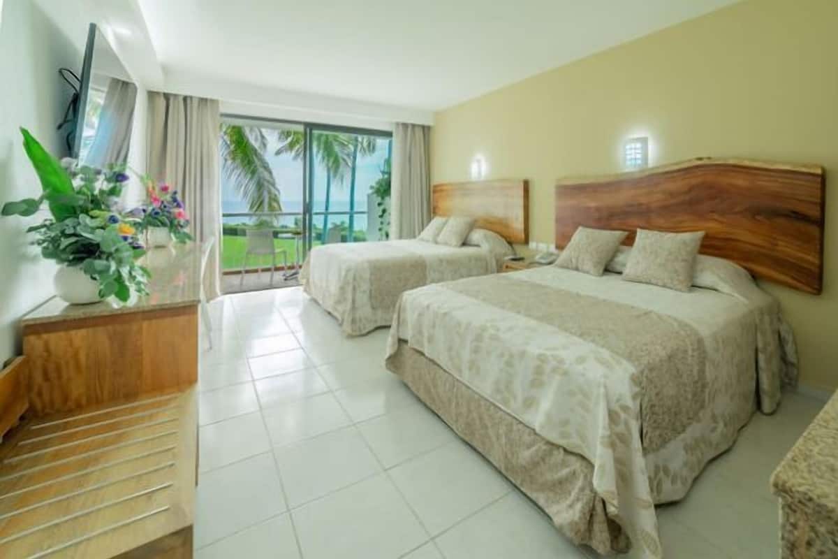 A hotel room with two beds, a balcony with a view, a TV, and a plant.