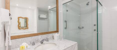 Un baño moderno con lavamanos de mármol, un espejo grande y ducha con cerramiento de vidrio.
