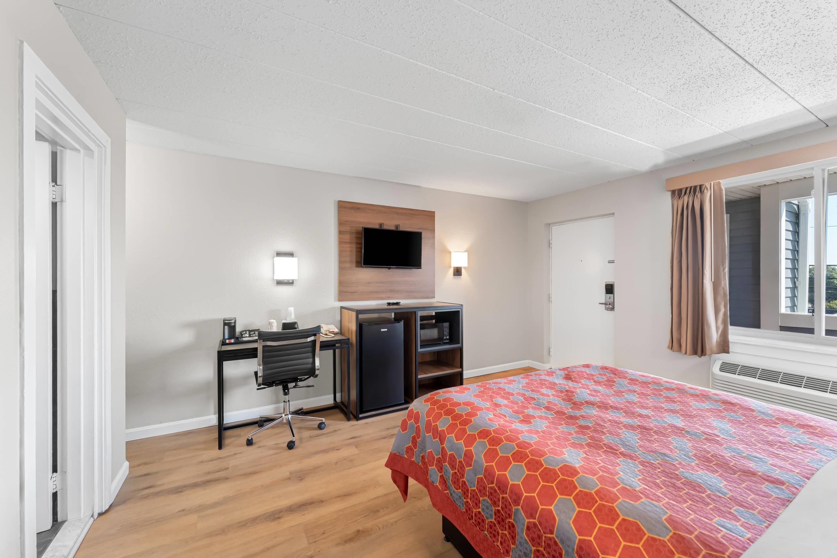 Une chambre d’hôtel avec un lit, un bureau, une chaise, une télévision et une fenêtre avec des rideaux.