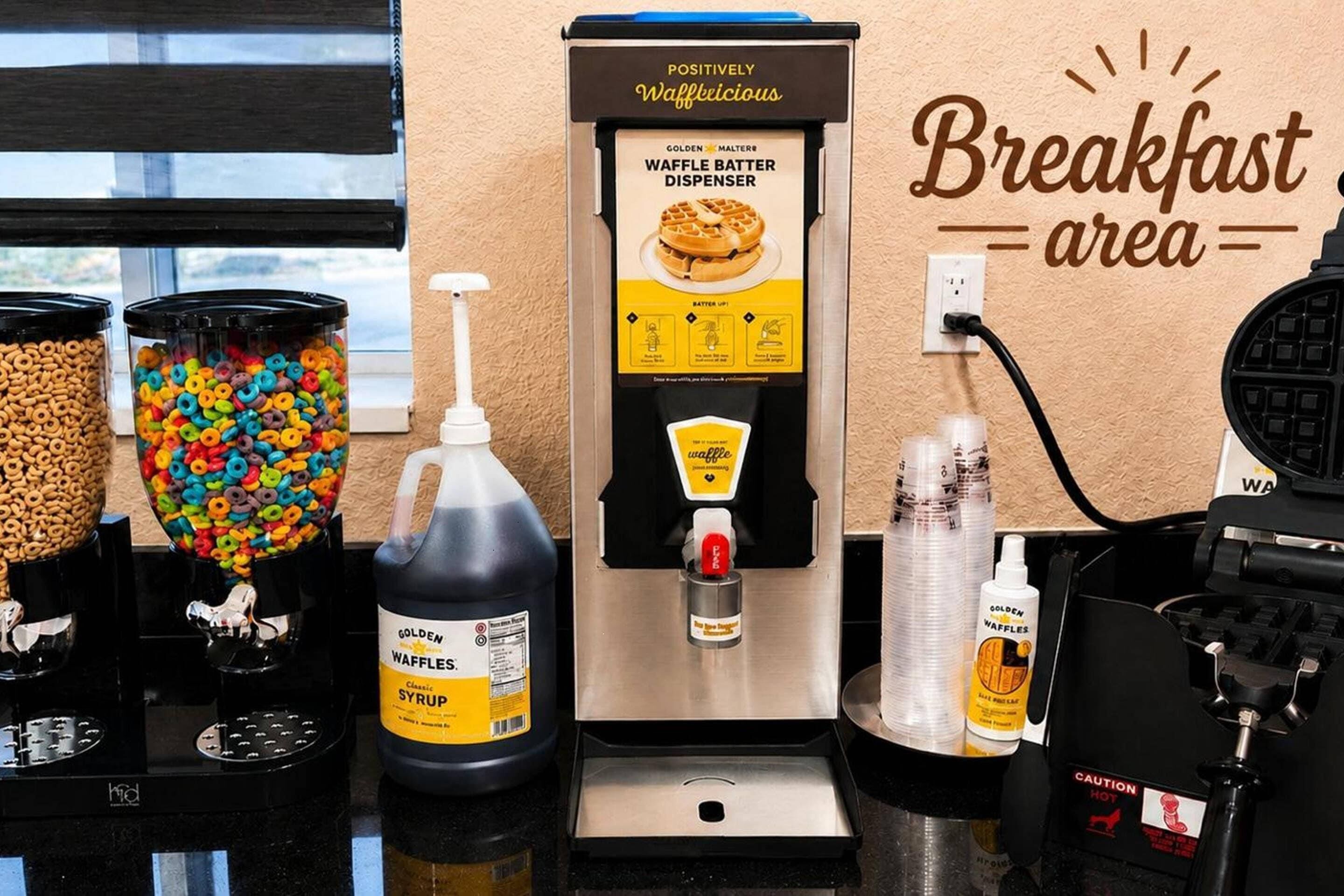 Un espace dédié au petit-déjeuner, équipé d’un distributeur de pâte à gaufres, de distributeurs de céréales et de bouteilles de sirop pour gaufres.