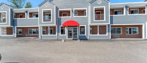 A multi-story building with a central entrance, multiple windows, and a red awning.