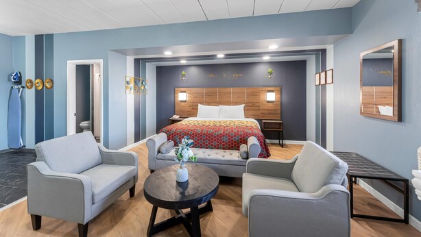 A modern hotel room with a large bed, two armchairs, a small table, and a mirror. - Econo Lodge Cranston - Providence (Cranston)