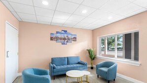 A room with a peach-colored wall, a blue sofa, two blue armchairs, a round table with gold legs, and a cityscape painting. - Econo Lodge Cranston - Providence (Cranston)