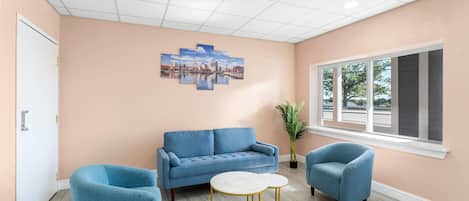 Une pièce avec un mur de couleur pêche, un canapé bleu, deux fauteuils bleus, une table ronde aux pieds dorés et un tableau représentant un paysage urbain.