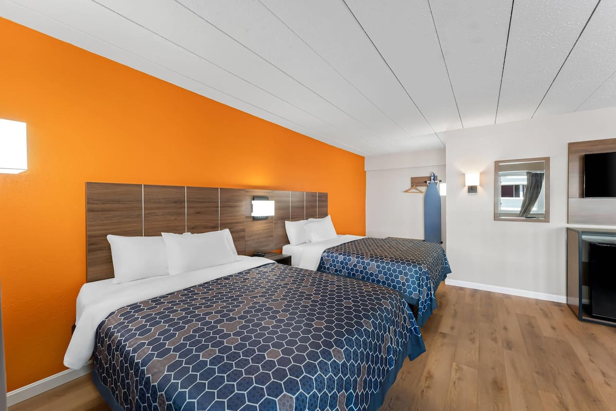 A hotel room with two beds, an orange wall, wooden headboard, and a TV.