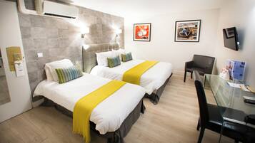 A hotel room with two beds, a desk, a chair, and a TV on the wall.