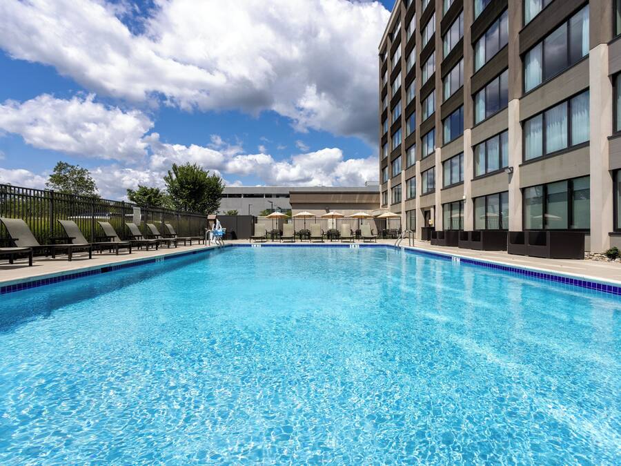 A swimming pool with lounge chairs and umbrellas, surrounded by a tall building with multiple windows.