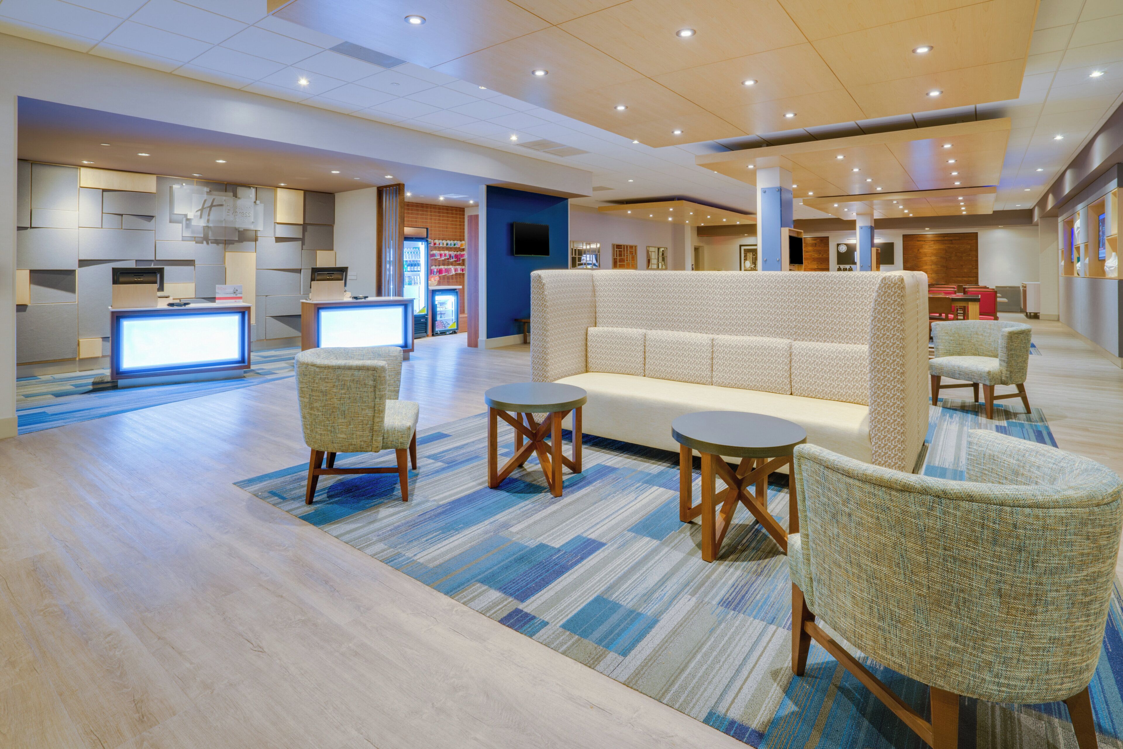 A hotel lobby with a reception desk, seating area, and a kitchenette.
