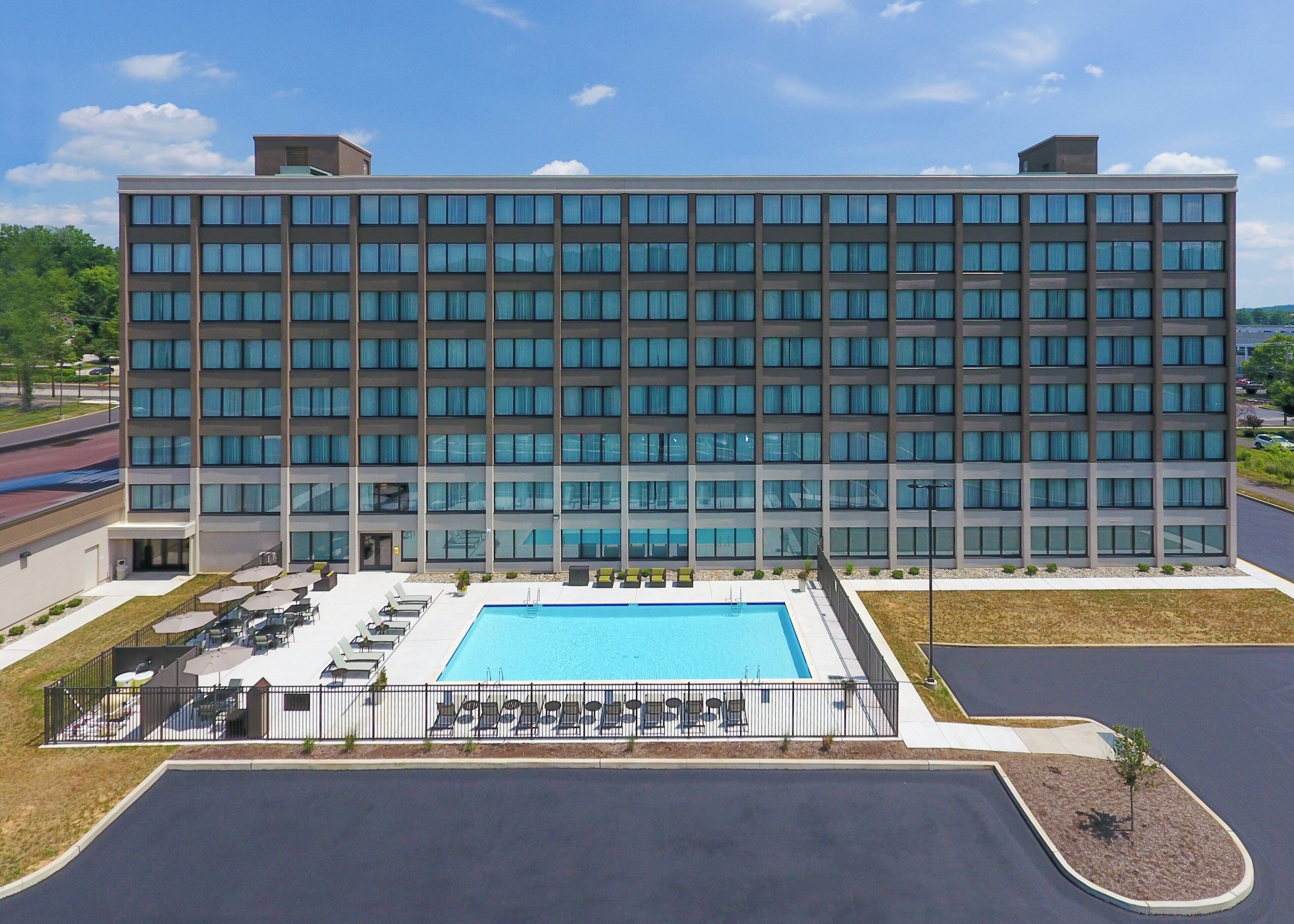 A modern hotel with a large pool area, outdoor seating, and a parking lot.