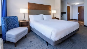 A hotel room with a large bed, a chair, two bedside tables with lamps, and a wooden headboard.